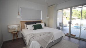 Quarto moderno com uma cama grande, vista para a piscina exterior e porta de correr para o pátio.