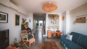 A living room with a sofa, a wicker chair, a TV, and a decorative wall hanging. - Kaz Lagoon, quiet house, sea view, 1mn walk from the lagoon! (Saint Paul)
