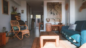 A living room with a blue sofa, a wooden coffee table, and a wicker chair. There is a wooden cabinet and a wall with a poster. - Kaz Lagoon, quiet house, sea view, 1mn walk from the lagoon! (Saint Paul)