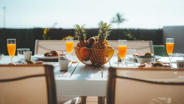 A breakfast table with a fruit bowl, glasses of orange juice, and plates of food. - Kaz Lagoon, quiet house, sea view, 1mn walk from the lagoon! (Saint Paul)