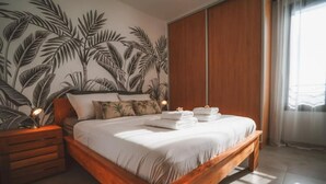 A bedroom with a wooden bed, a nightstand, a wall mural, and a window with curtains. - Kaz Lagoon, quiet house, sea view, 1mn walk from the lagoon! (Saint Paul)