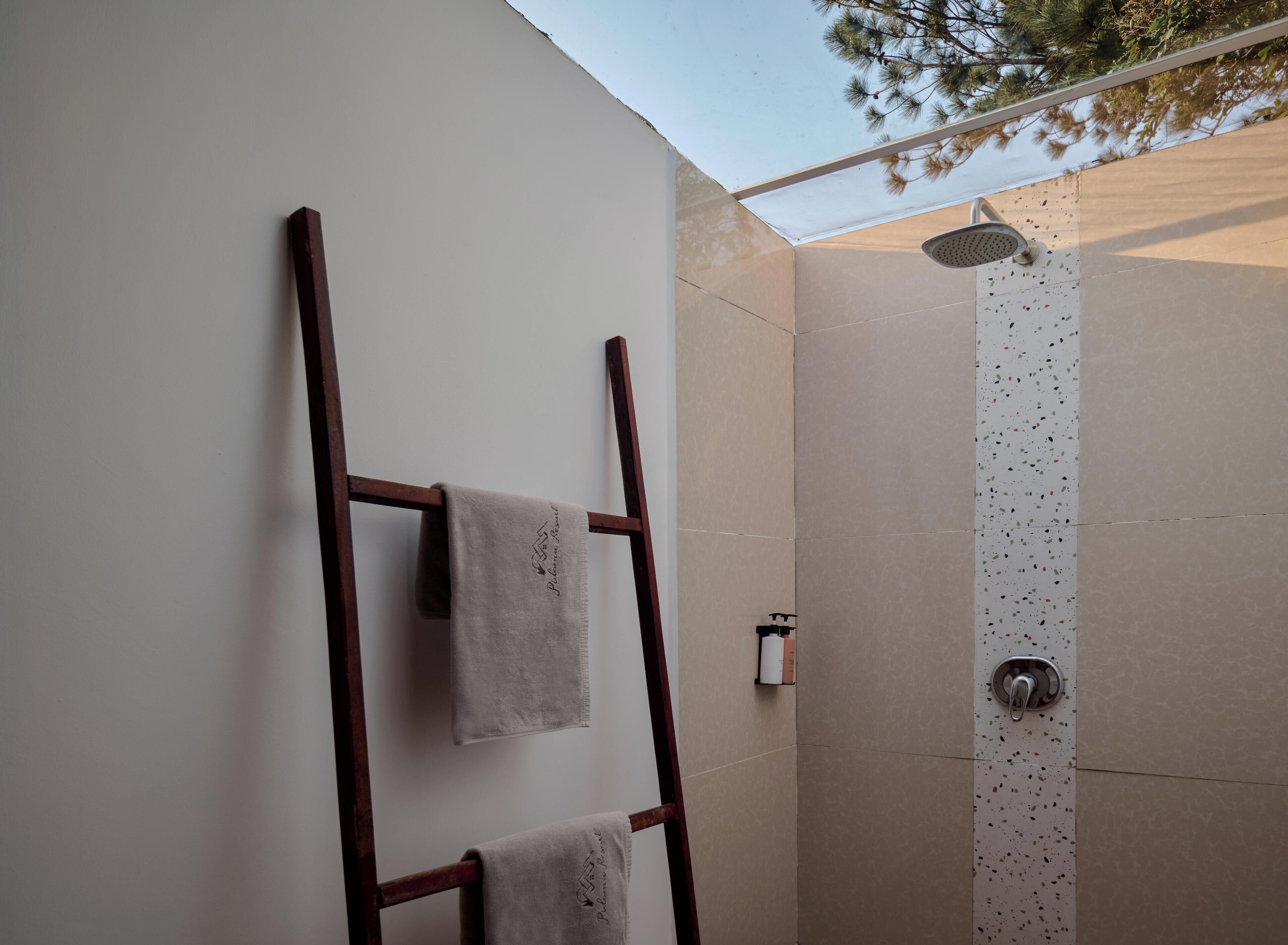 A shower with a speckled wall, a wooden ladder, and two towels hanging on the wall.
