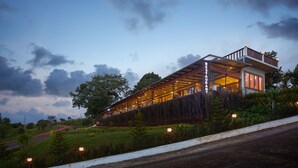 Un edificio moderno con techo inclinado y un balcón, rodeado de abundante vegetación.