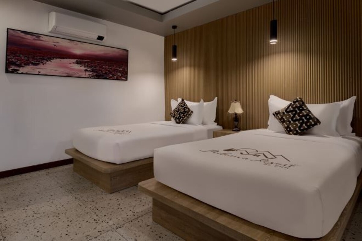 A hotel room with two beds, a painting on the wall, and a wooden panel design.