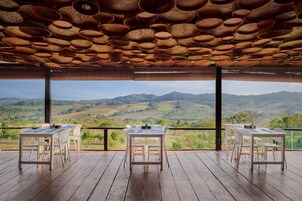 A terrace with wooden flooring, white tables and chairs, and a view of green hills.