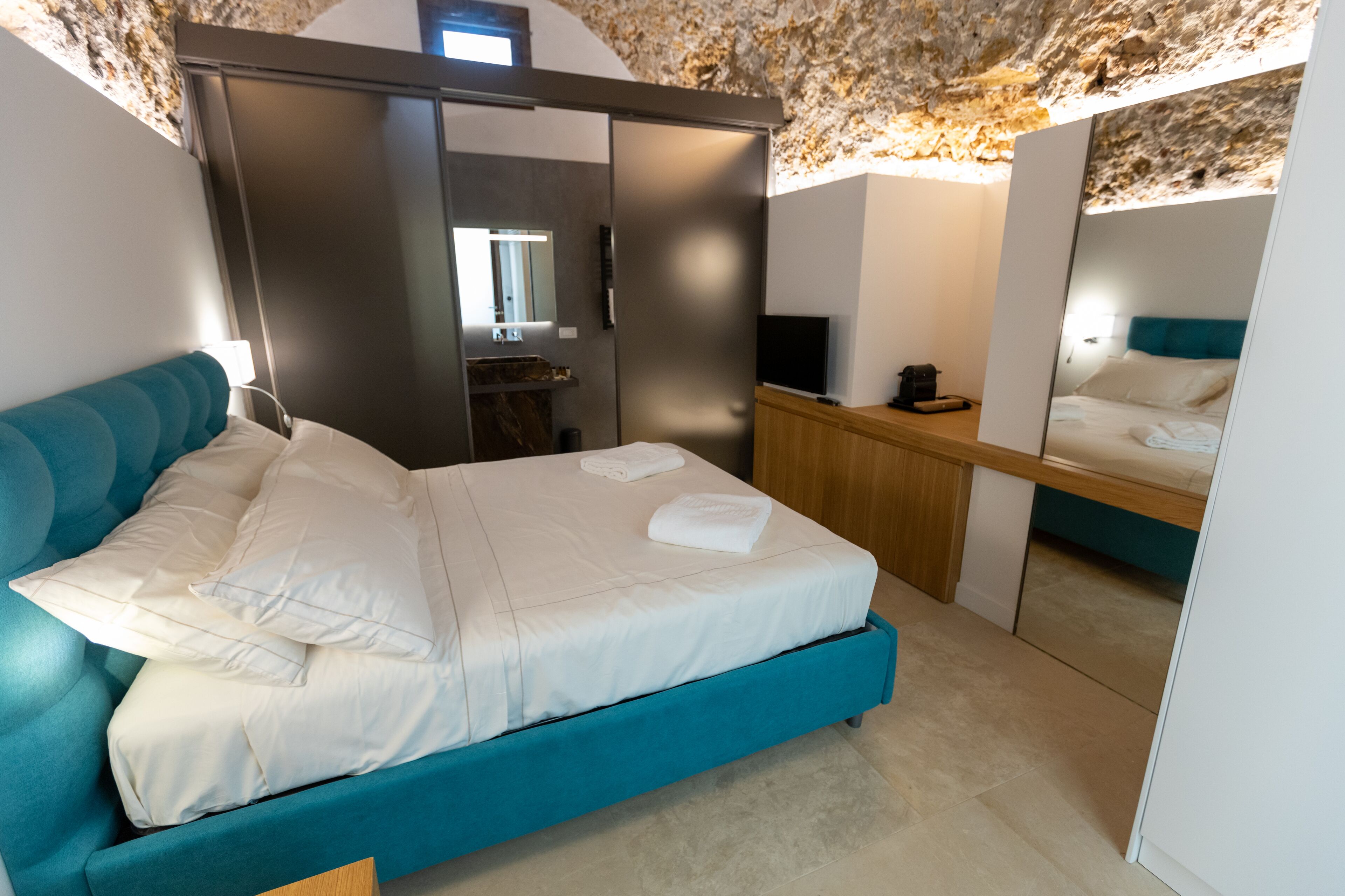 A bedroom with a bed, a wardrobe, a desk, and a mirror.