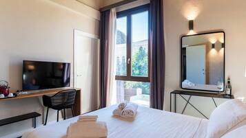 Quarto de hotel com cama, escrivaninha com televisão, poltrona, janela com cortinas e espelho.