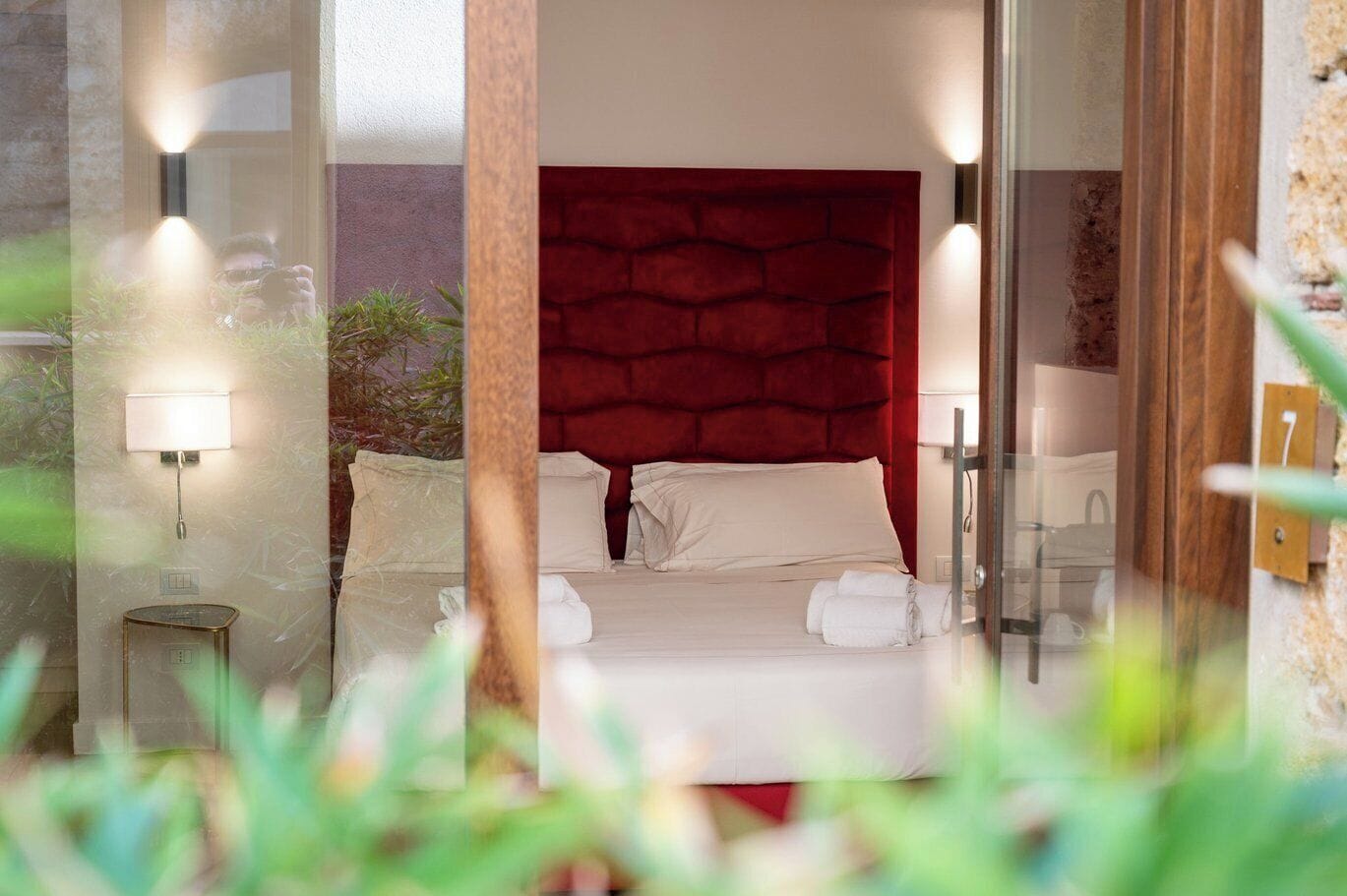 A bedroom with a red headboard, a bed with white linens, two bedside lamps, and a small bedside table.