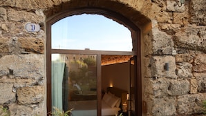 Una habitación con paredes de piedra, una cama, una mesita de noche y una ventana.