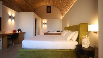 Une chambre d’hôtel avec un plafond en briques, un lit recouvert d’un tissu vert, un bureau avec une chaise et une salle de bain équipée d’un lavabo et d’un miroir.