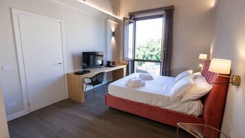 Une chambre d’hôtel comprenant un lit, un bureau avec une chaise, une télévision et une fenêtre avec des rideaux.