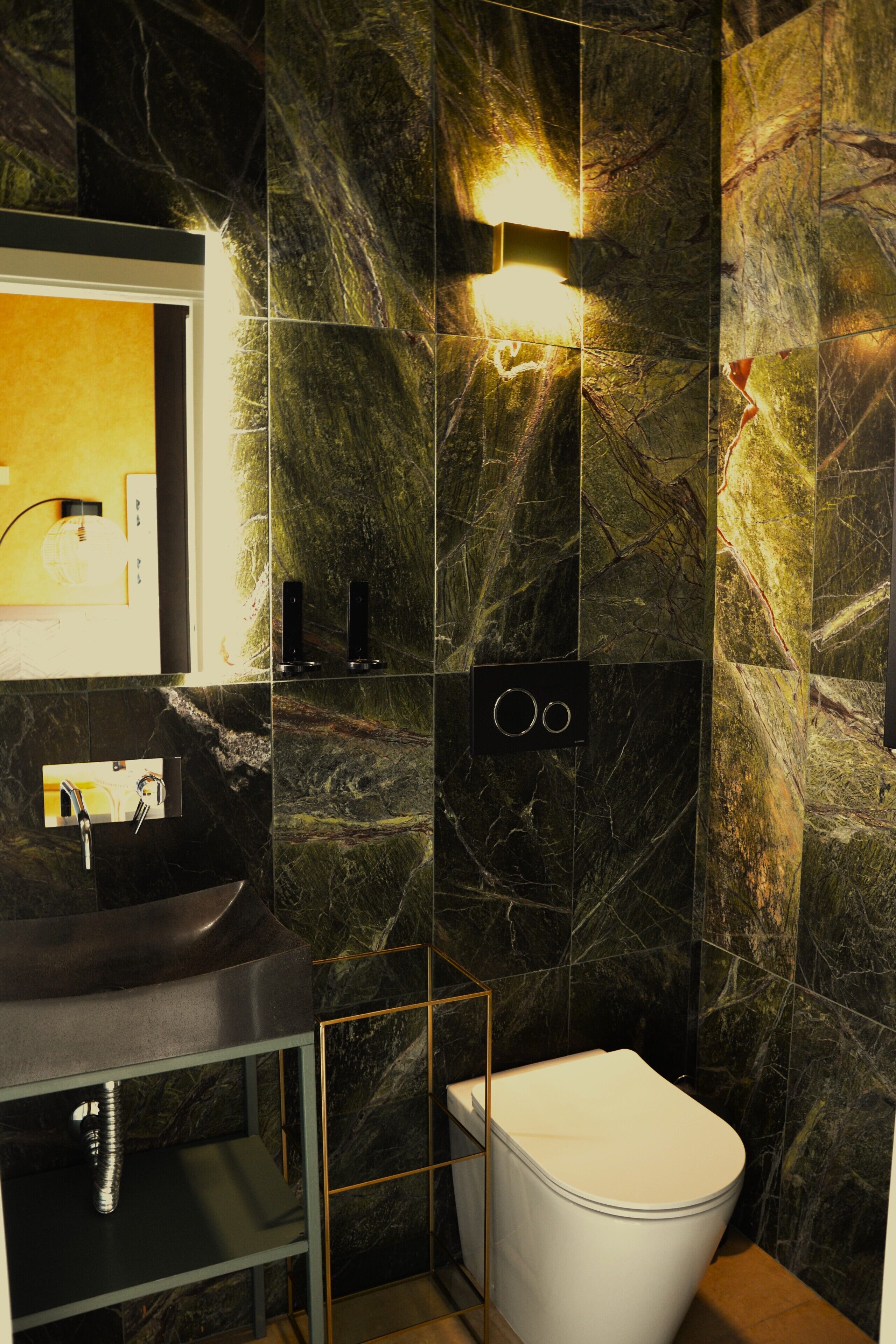 A modern bathroom with a marble wall, a black sink, a white toilet, and a mirror.