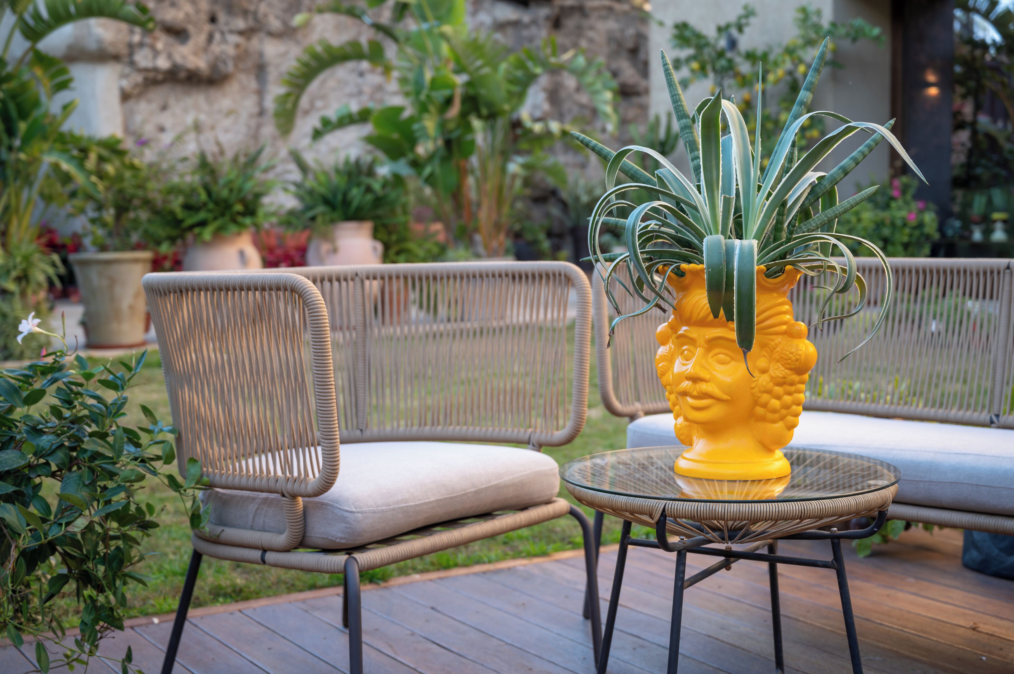 Un conjunto de sillones y sofá de mimbre sobre una terraza de madera, con una planta en maceta y un adorno amarillo.