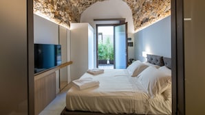 Un dormitorio moderno con techo de piedra, un televisor de pantalla plana, una cama con sábanas blancas y vistas a la vegetación.