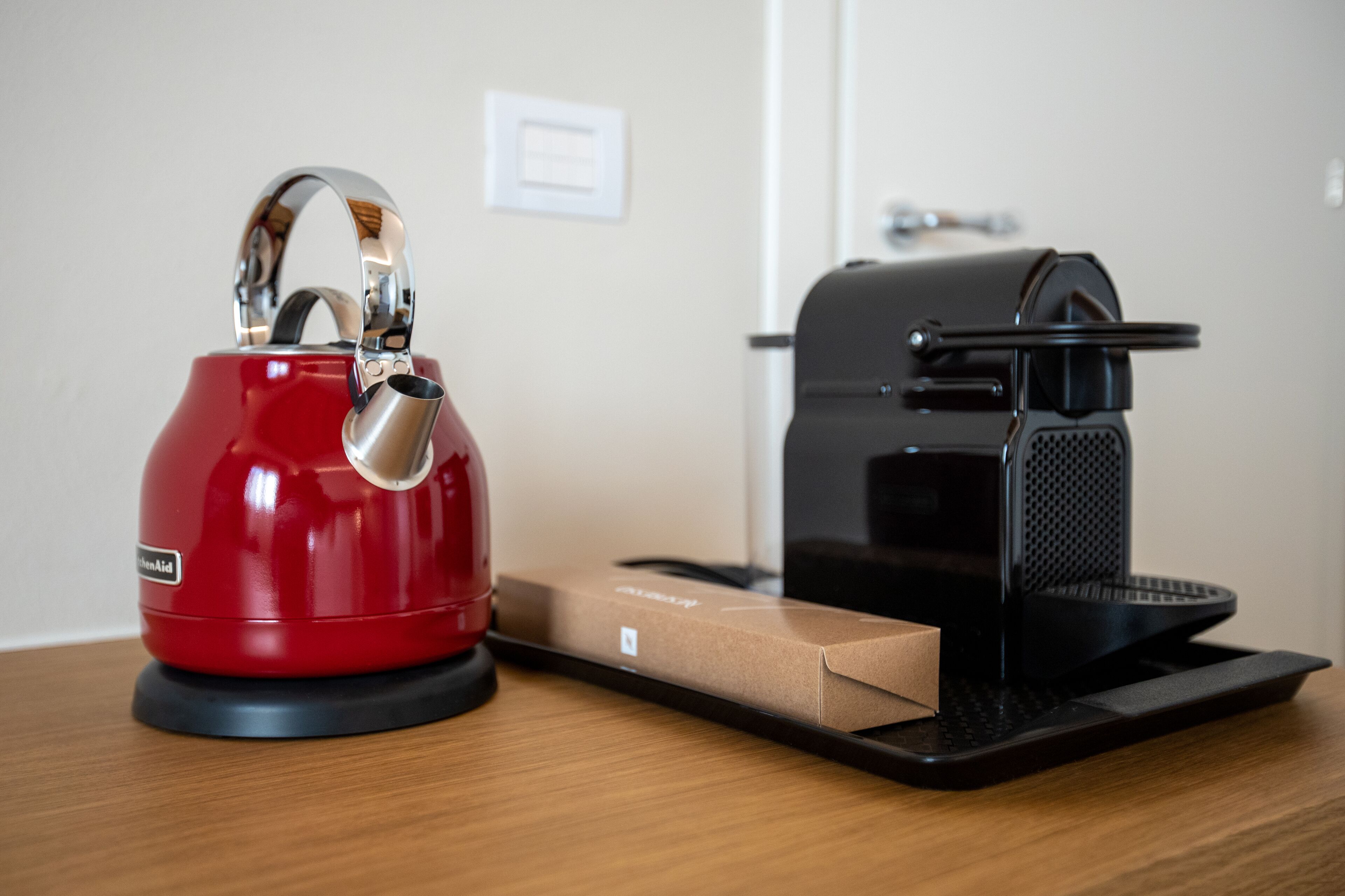 A red kettle, a black coffee machine, and a cardboard box on a wooden table.