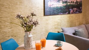 A dining area with a round table, chairs, a vase with flowers, a glass of orange juice, a cup of coffee, and a plate with food.