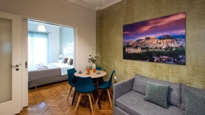 A modern hotel room with a dining area, a sofa, and a large cityscape painting on the wall.
