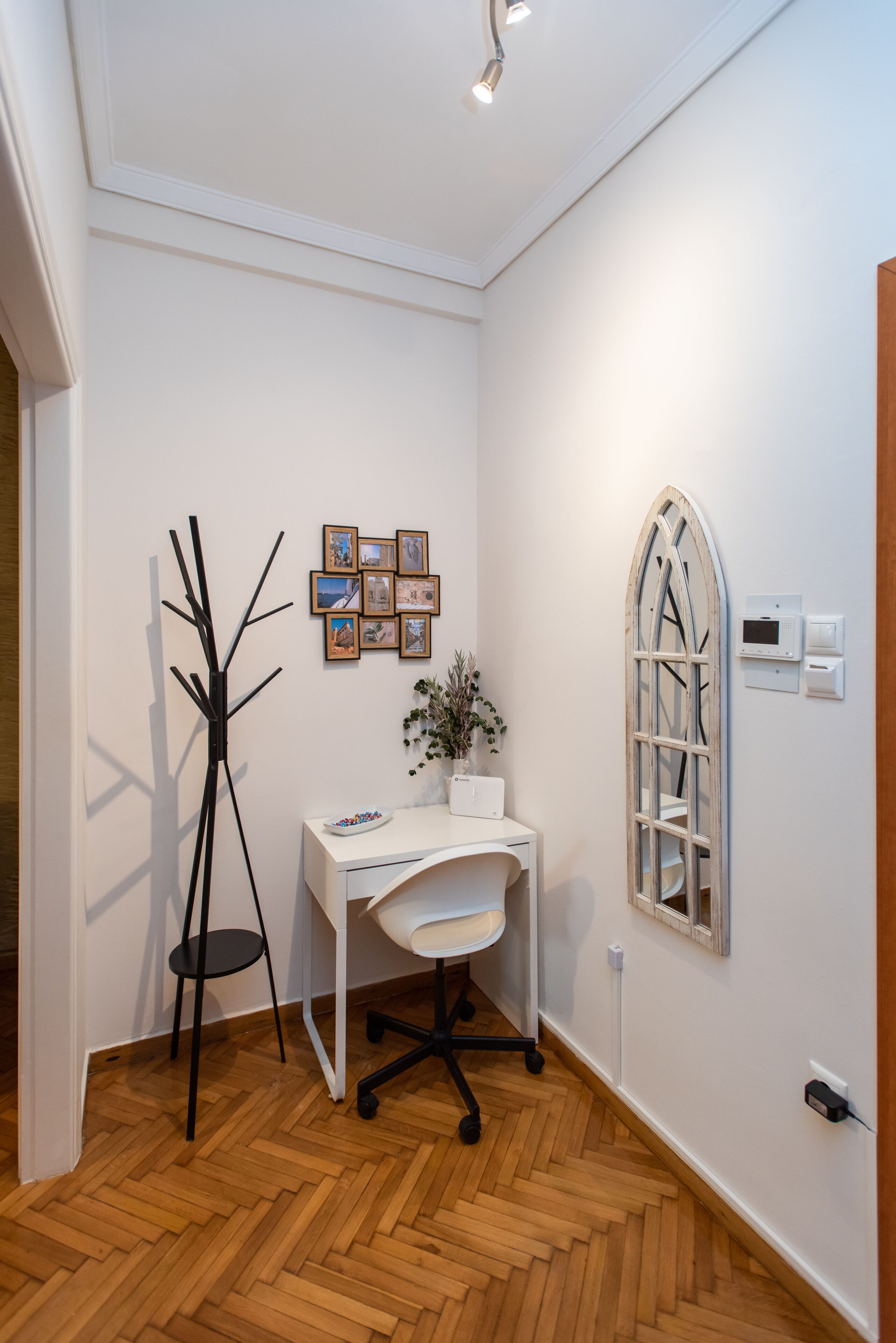 A small, well-lit room with a white desk, a chair, a coat rack, and a decorative window.