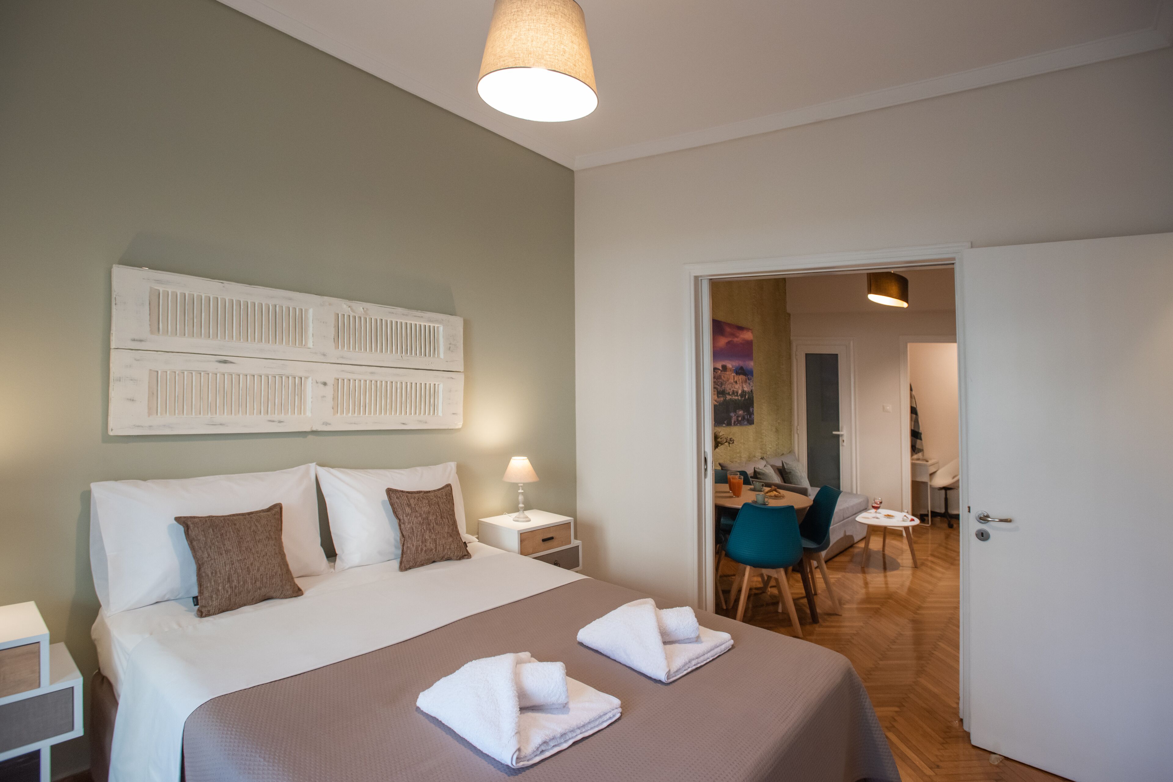 A neatly arranged hotel room with a large bed, a bedside table, a chair, and a small table with a lamp.