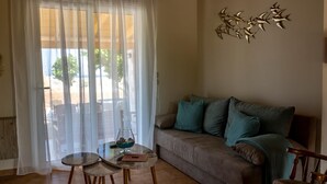 Una sala de estar con un sofá, dos mesitas, una mesa de centro de vidrio con adornos, una escultura en la pared y vistas a través de cortinas traslúcidas.