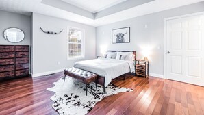 Une chambre à coucher comprenant un lit, un banc, un tapis, une commode, un miroir, une fenêtre et une porte.