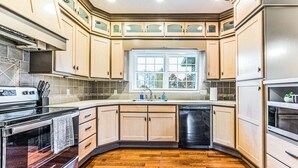 Une cuisine avec des meubles en bois, un lave-vaisselle, une cuisinière et une fenêtre donnant sur les arbres.