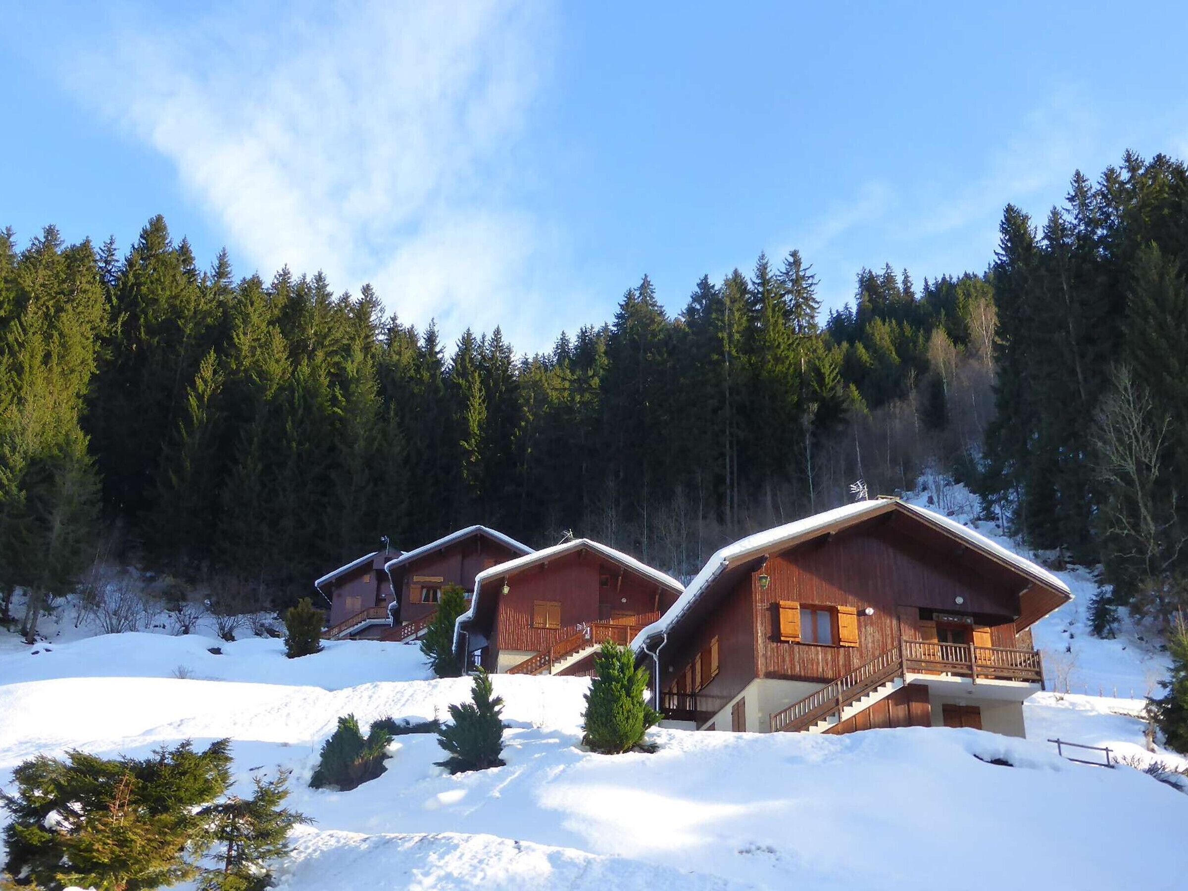 Uma fileira de cabanas de madeira com varandas, rodeadas por neve e uma floresta densa.