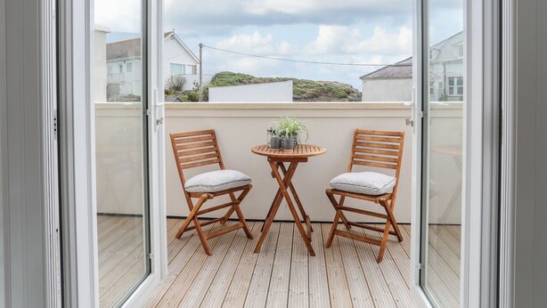 Een balkon met twee houten stoelen en een klein rond tafeltje, met een bloempot.