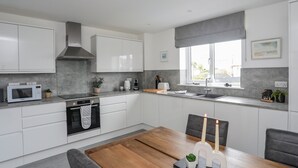 Een moderne keuken met witte kastjes, een inbouwoven, een magnetron en een groot raam met uitzicht.