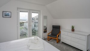 Een slaapkamer met een bed, een stoel, een kaptafel en uitzicht door een glazen deur.