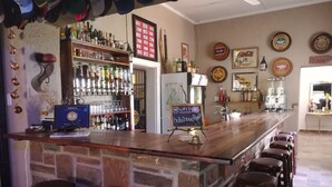 A bar area with a stone counter, stools, and a variety of bottles and glasses. - Bethanie Hotel and Guesthouse (Bethanie)