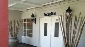 A reception area with a closed door, a window, and two potted plants with sticks. - Bethanie Hotel and Guesthouse (Bethanie)