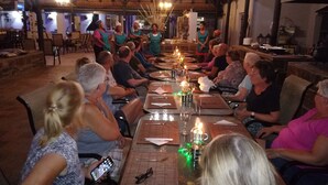 A group of people seated around a long table in a rustic dining area with wooden beams and hanging lights. - Bethanie Hotel and Guesthouse (Bethanie)