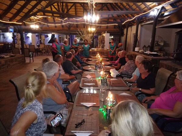 A group of people seated around a long table in a rustic dining area with wooden beams and hanging lights.