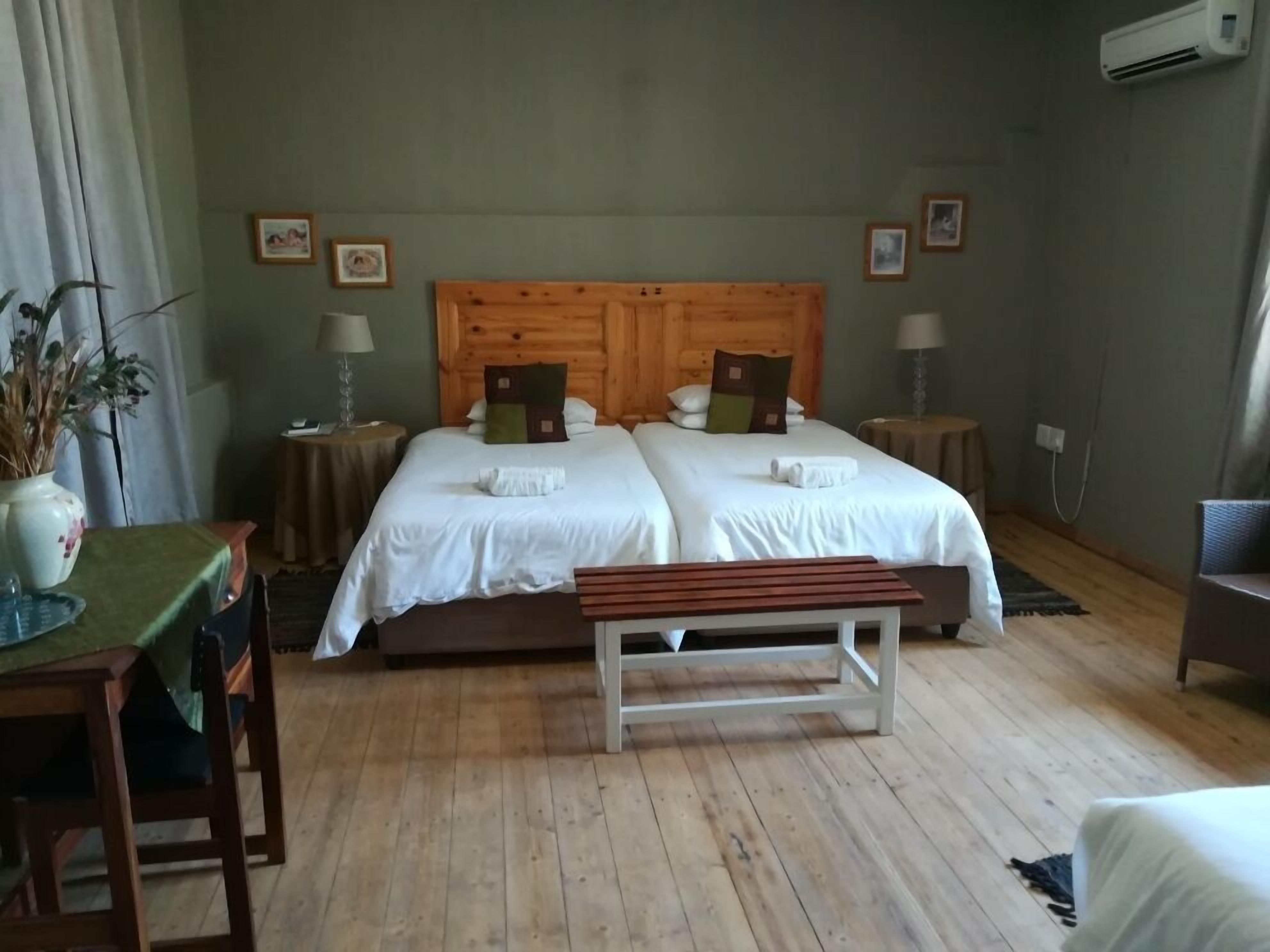 Habitación doble con dos camas, cabecera de madera, mesitas de noche con lámparas, un banco y una planta en maceta.
