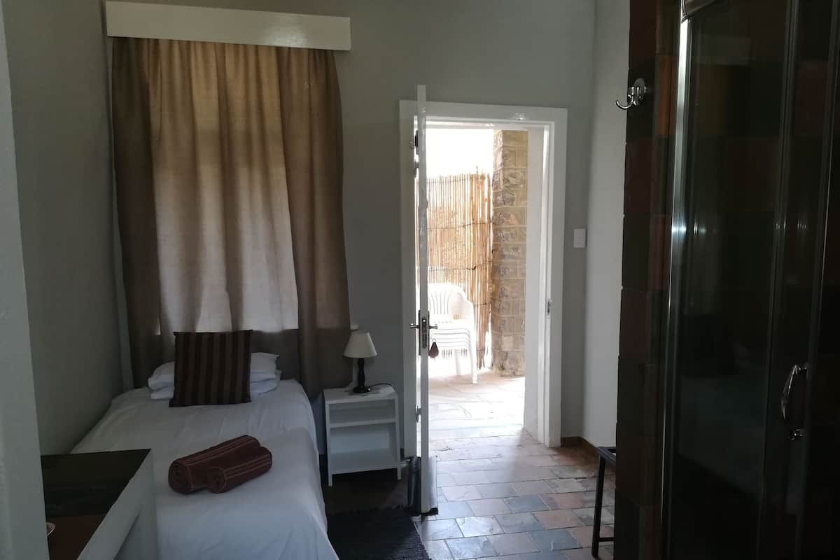 Une chambre d’hôtel comprenant un lit, une table de chevet, une lampe et une vue sur un espace extérieur aménagé avec une chaise et une table.