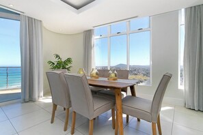 Ein Essbereich mit Tisch und Stühlen, großen Fenstern mit Aussicht und einem Blumentopf.