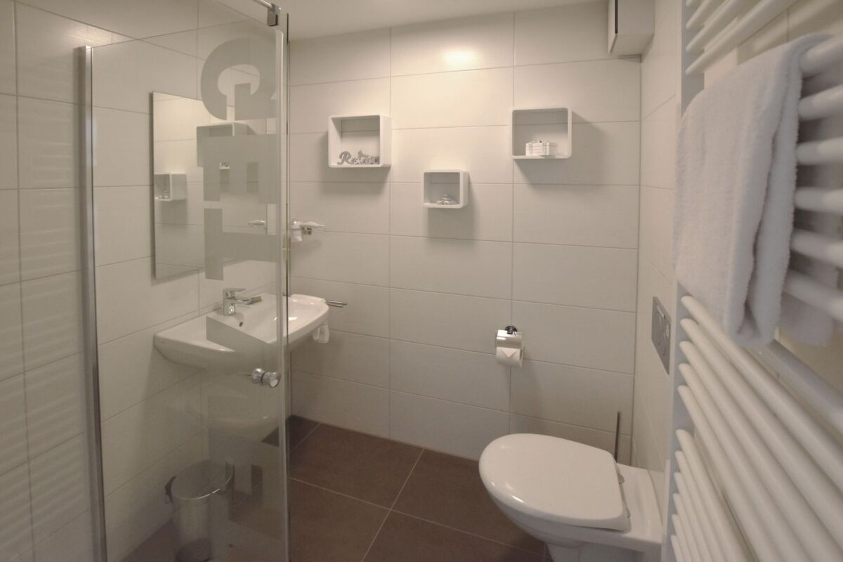 Een badkamer met een douchecabine van glas, een witte wastafel, een toilet en een handdoekrek.