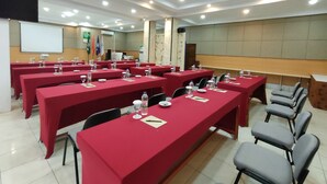 A conference room with red tables, chairs, and a projector screen. - Golden Ganesha Hotel Yogyakarta by Ecommerceloka (Banguntapan)