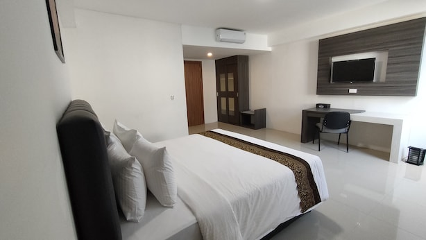 A modern hotel room with a large bed, a desk, and a TV mounted on the wall. - Golden Ganesha Hotel Yogyakarta by Ecommerceloka (Banguntapan)