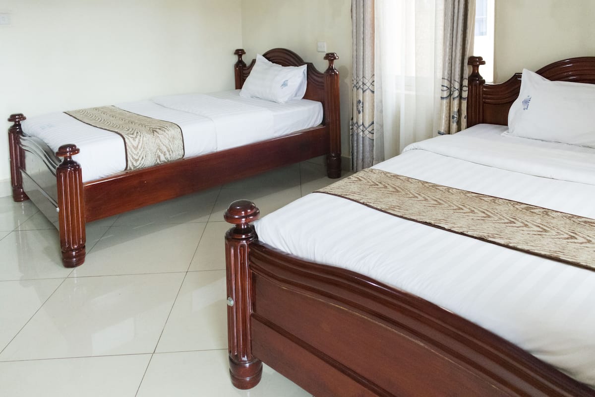 Two wooden beds with white linens and decorative pillows, a tiled floor, and a window with curtains.