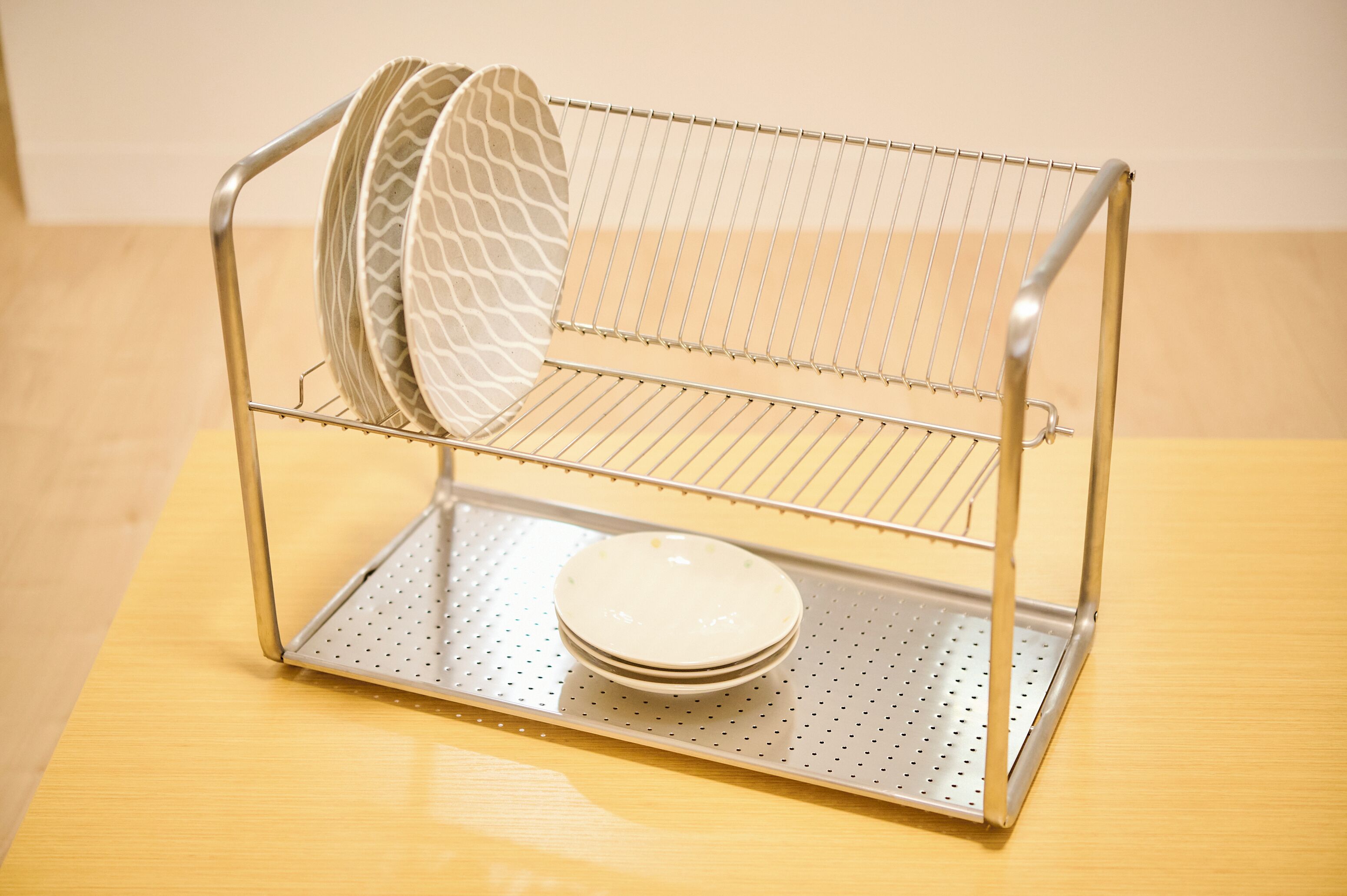 A metal drying rack with plates and a patterned plate on it, placed on a wooden surface.