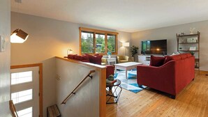 Ett modernt vardagsrum med en röd soffa, ett vitt soffbord och en tv. En trappa med ett ledstång leder upp till en annan våning.