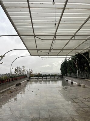 A covered outdoor area with a tiled floor, metal framework, and hanging light bulbs. - Dora Residence (Tirana)