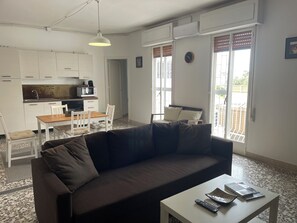 A living room with a dark brown sofa, a white coffee table, and a kitchen area with white cabinets and a microwave.