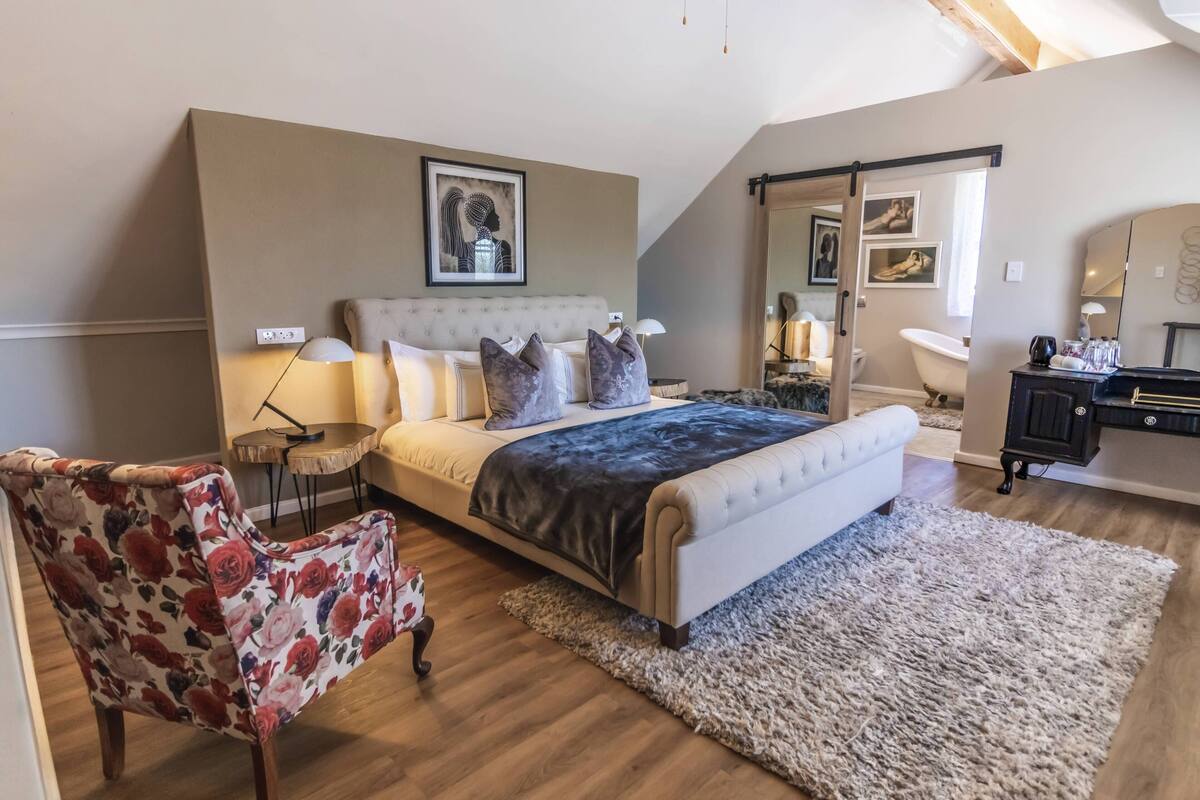 Een slaapkamer met een groot bed, een stoel, een bureau en een bad.