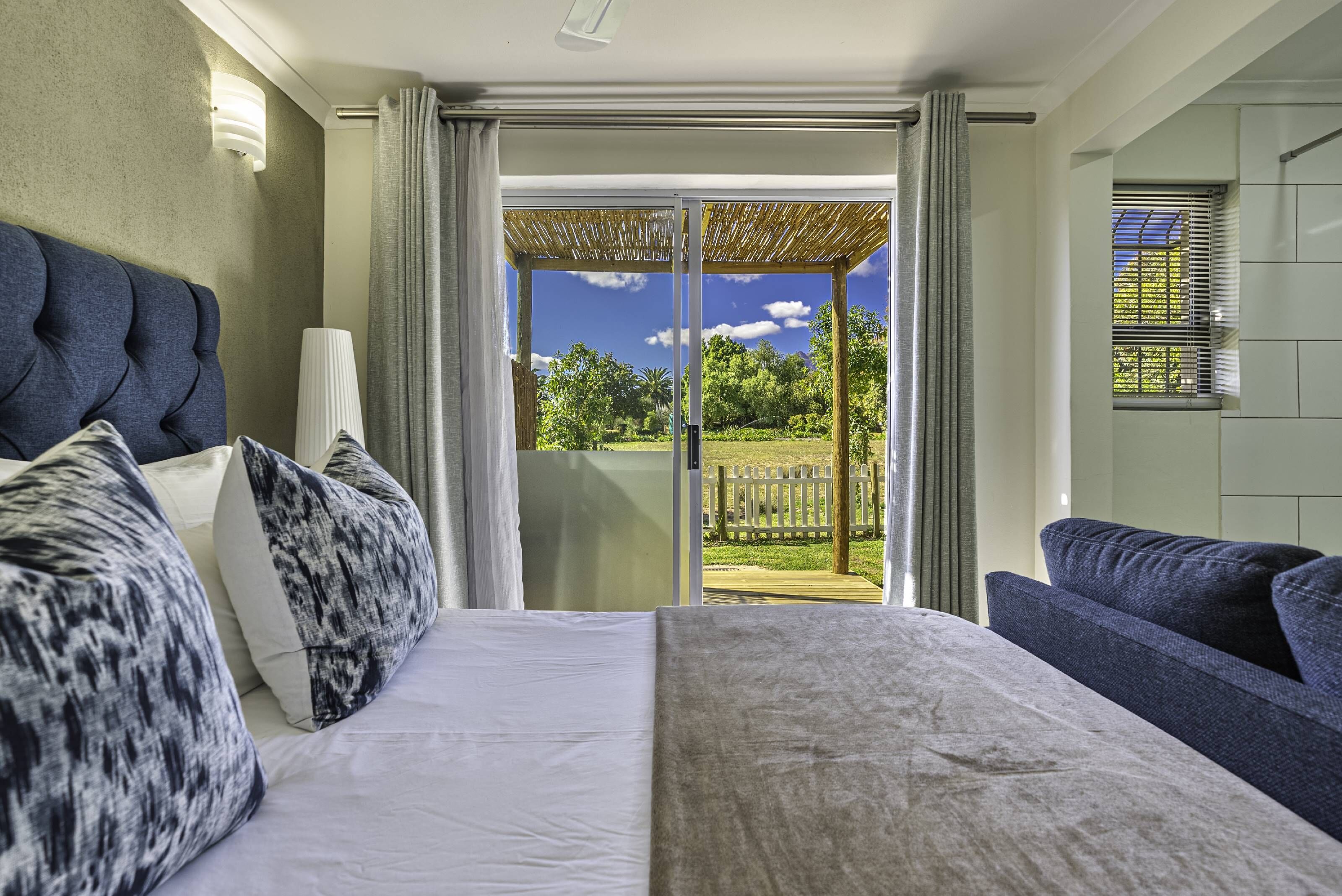 A hotel room with a bed, a sofa, a view of a garden, and a sliding glass door.