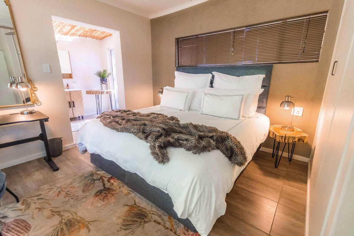 Een slaapkamer met een groot bed, een nachtkastje, een spiegel en een klein bijzettafeltje met een lamp.