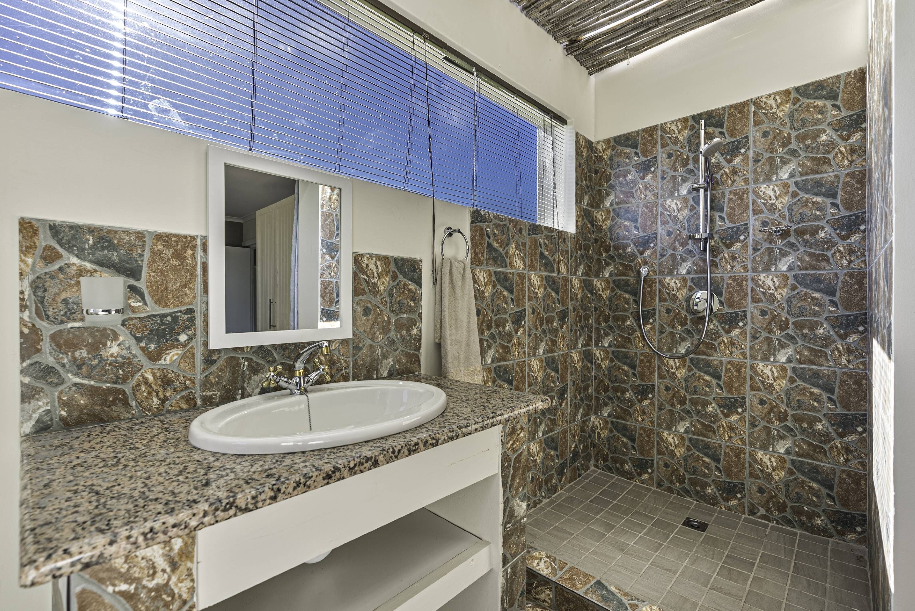 Une salle de bain avec une douche en pierre, un lavabo doté d’un plan de travail en granit et un miroir au-dessus du lavabo.
