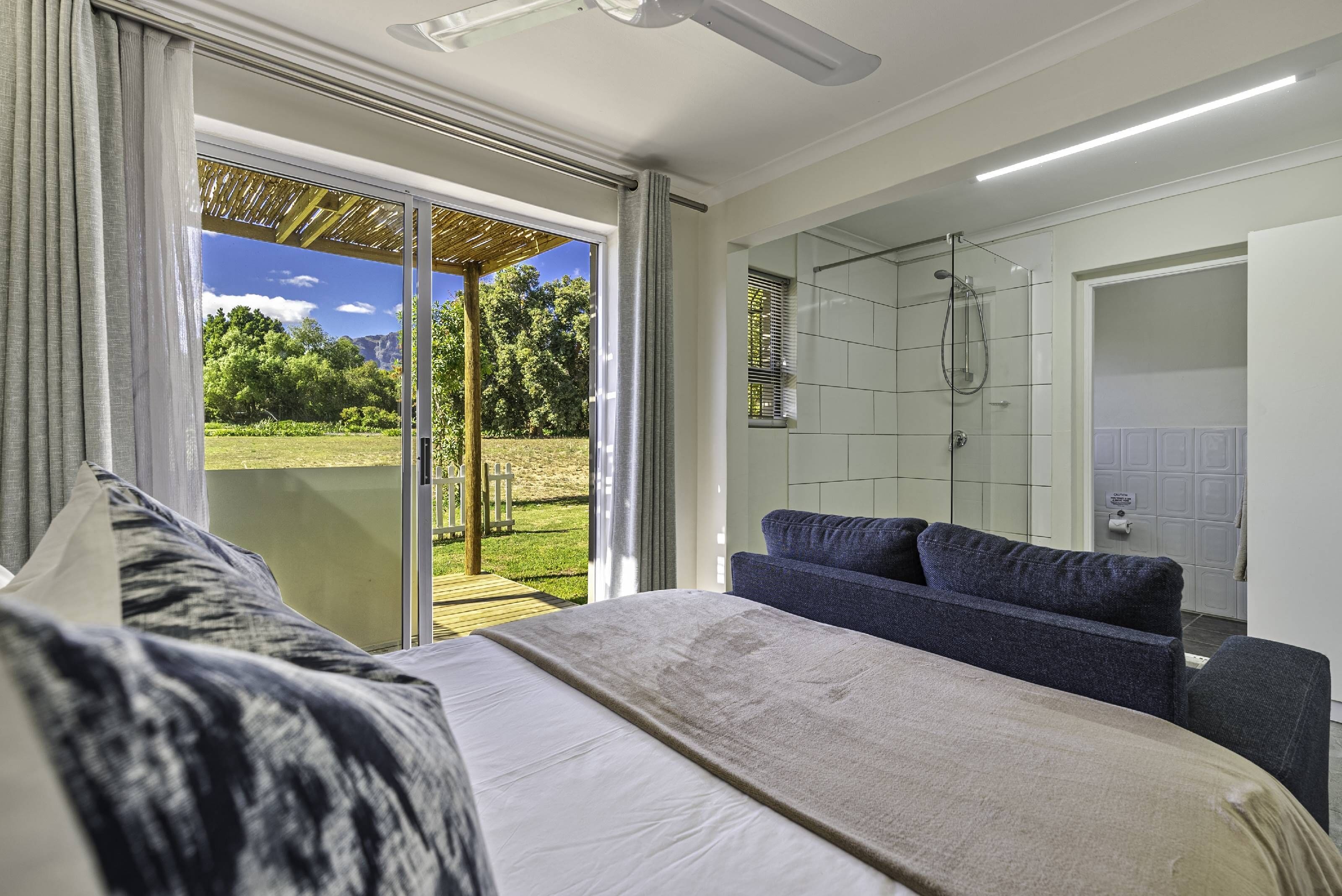 A bedroom with a large bed, a sofa, a sliding glass door to a balcony, and a shower area.